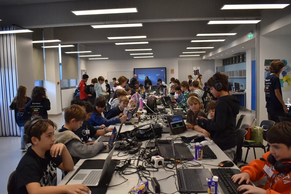A long room of students working at laptops at shared tables