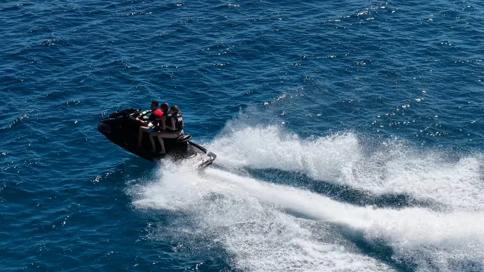 Aerial view of three riders on a jet ski carving a wake across open sea